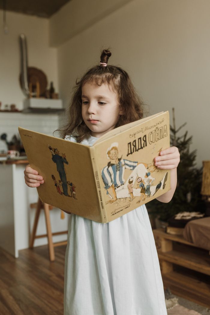 Services Young girl reading a childrens book in a cozy indoor setting.